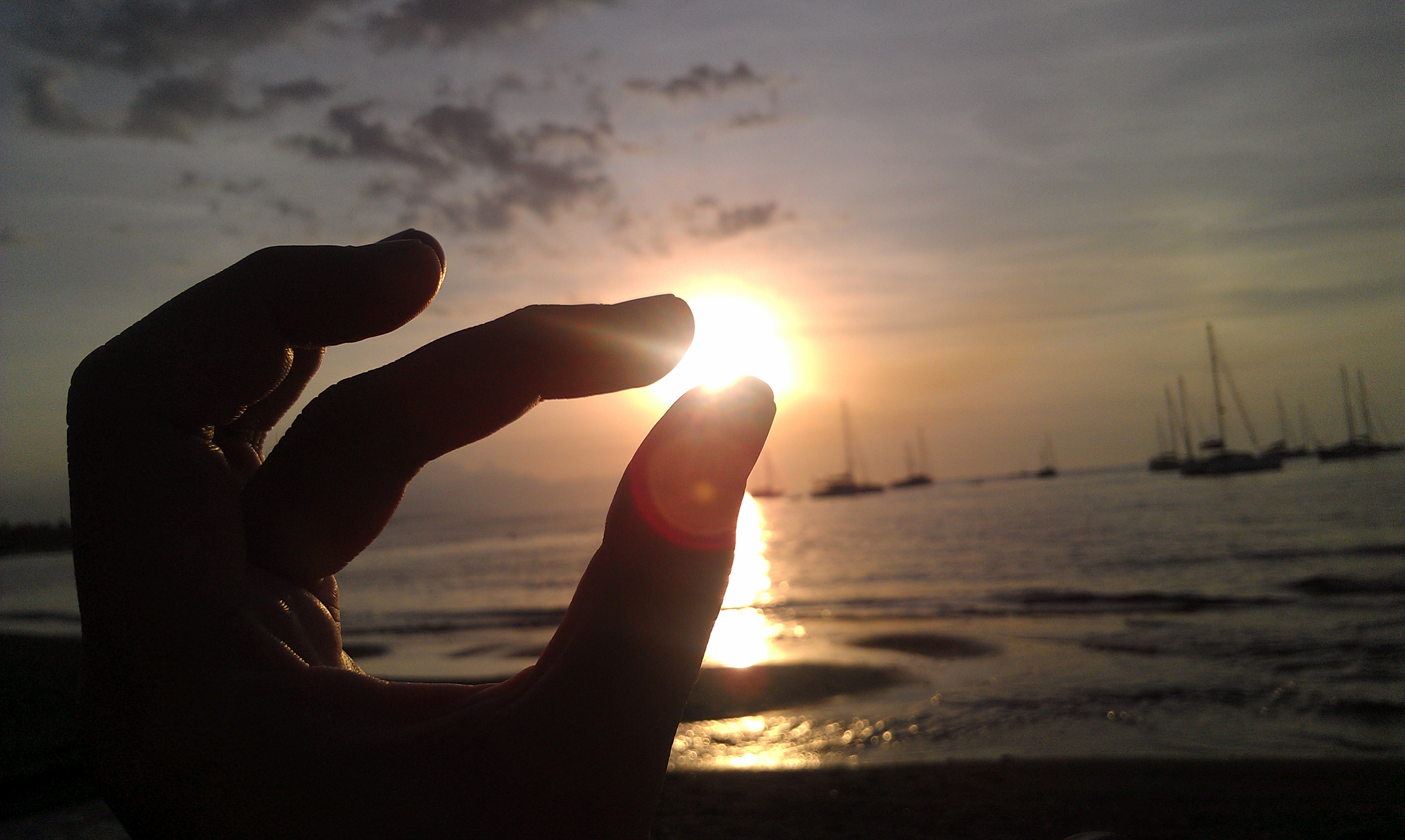 Hand pinching the sunset over calm water